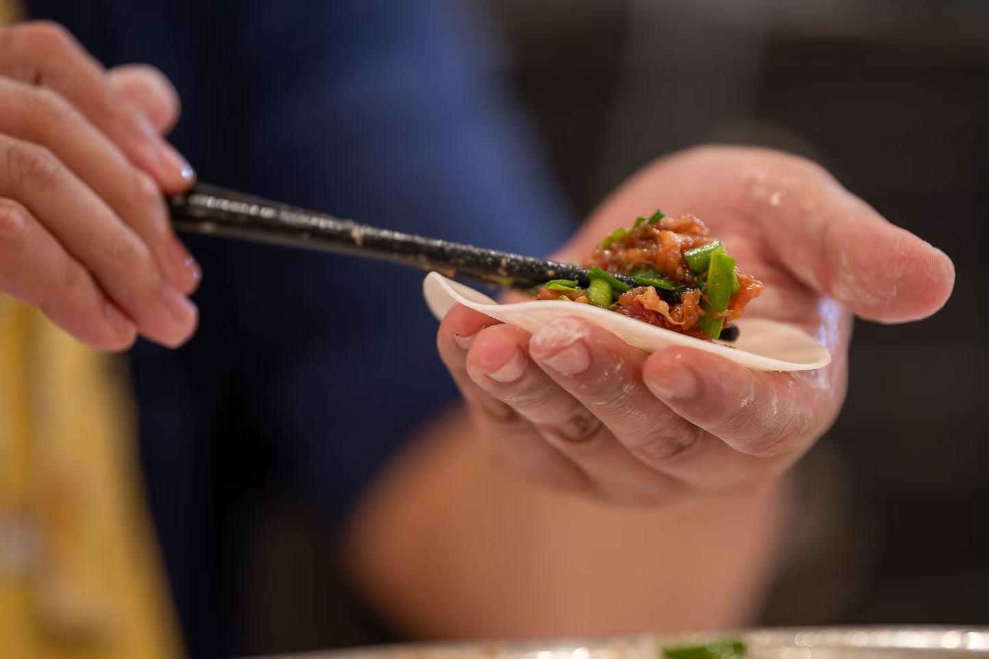 Hands folding a fresh dumpling wrapper