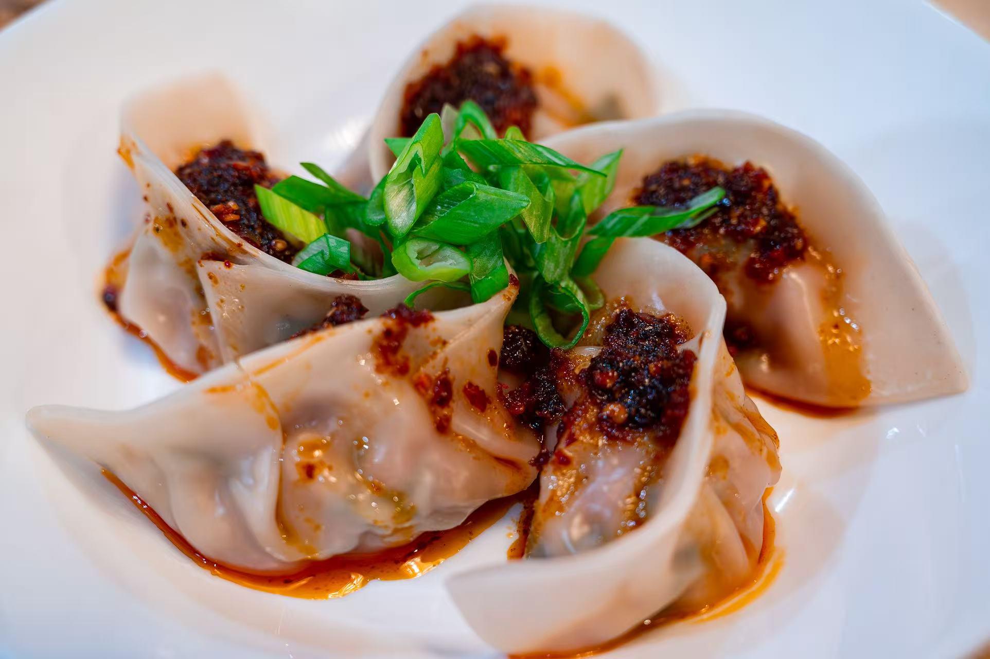 Handmade dumplings topped with chili oil and fresh scallions